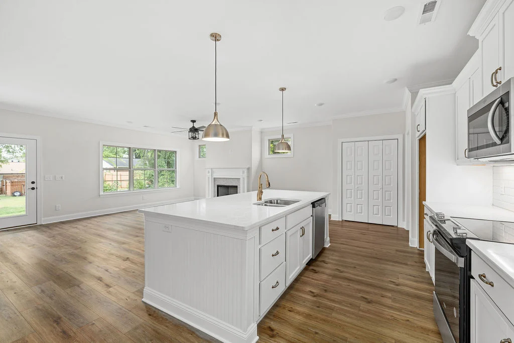 Modern kitchen with white cabinets and island, hardwood floors, stainless steel appliances, open to living area. Pratt Home Builders in Chattanooga TN