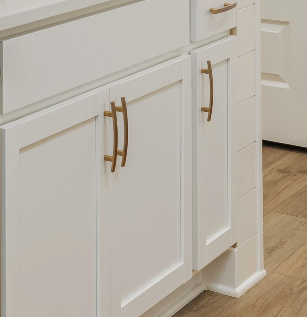 White kitchen cabinets with gold handles and wood flooring, showcasing modern design by Pratt Home Builders in Chattanooga TN.