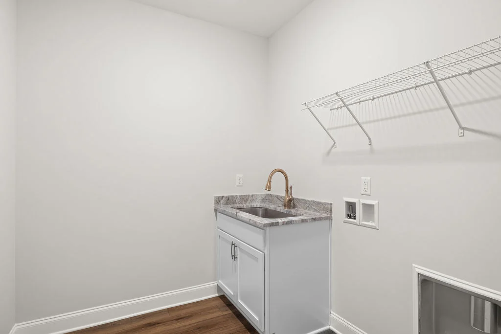 Laundry room with marble-topped sink, bronze faucet, white cabinet, and wire shelf. Designed by Pratt Home Builders in Chattanooga TN.
