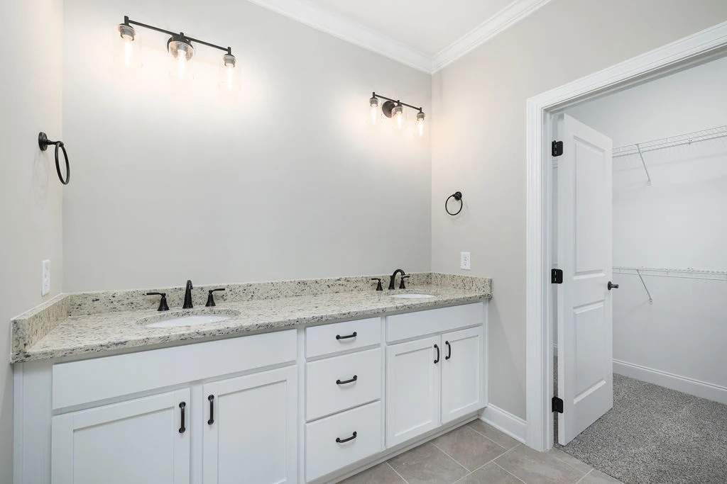 Bright bathroom by Pratt Home Builders in Chattanooga TN featuring dual sinks, white cabinets, granite countertops, and modern light fixtures.