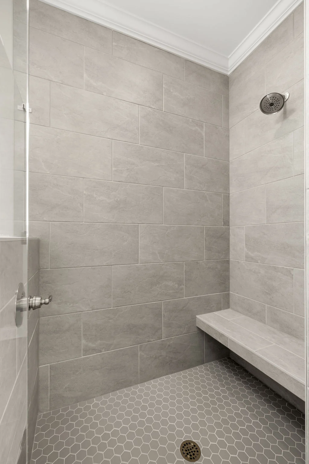 Modern shower with gray tiles, built-in bench, and hexagonal floor by Pratt Home Builders in Chattanooga TN.
