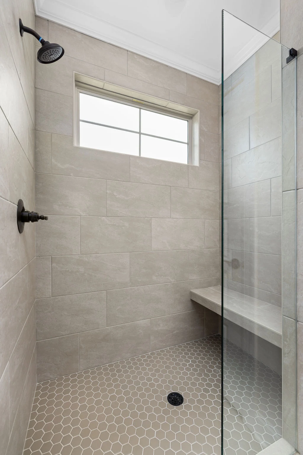 Modern shower with beige tile, glass door, bench, and hexagonal floor tiles by Pratt Home Builders in Chattanooga, TN.