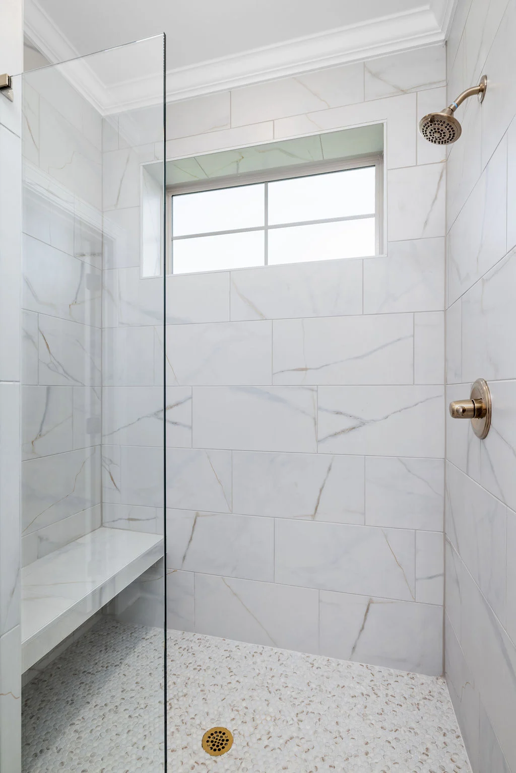 Marble-tile shower with glass door and window, featuring a rainfall showerhead and pebble floor. Designed by Pratt Home Builders in Chattanooga TN.