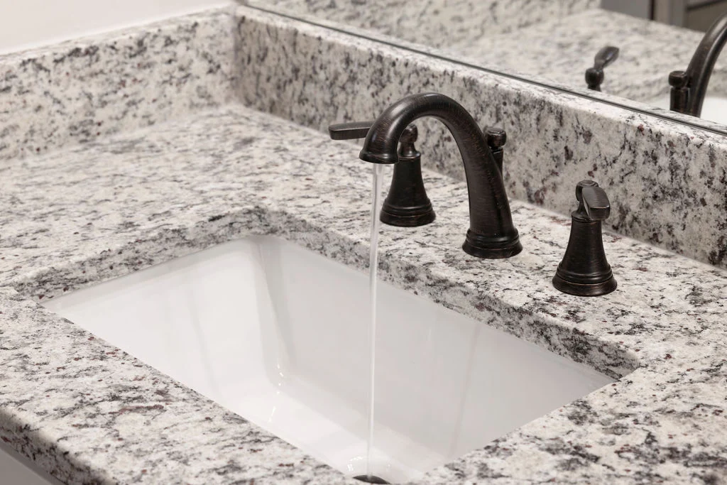 Modern bathroom sink with running water, dark bronze faucet, and granite countertop by Pratt Home Builders in Chattanooga TN.