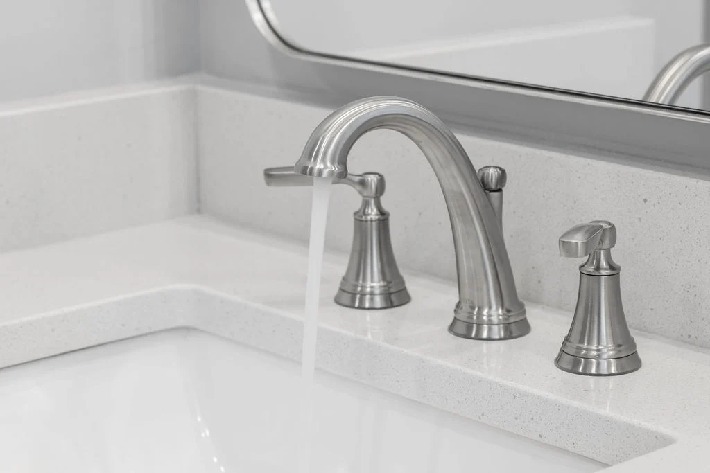 Modern chrome bathroom faucet with flowing water in a sleek, white granite countertop by Pratt Home Builders in Chattanooga TN.
