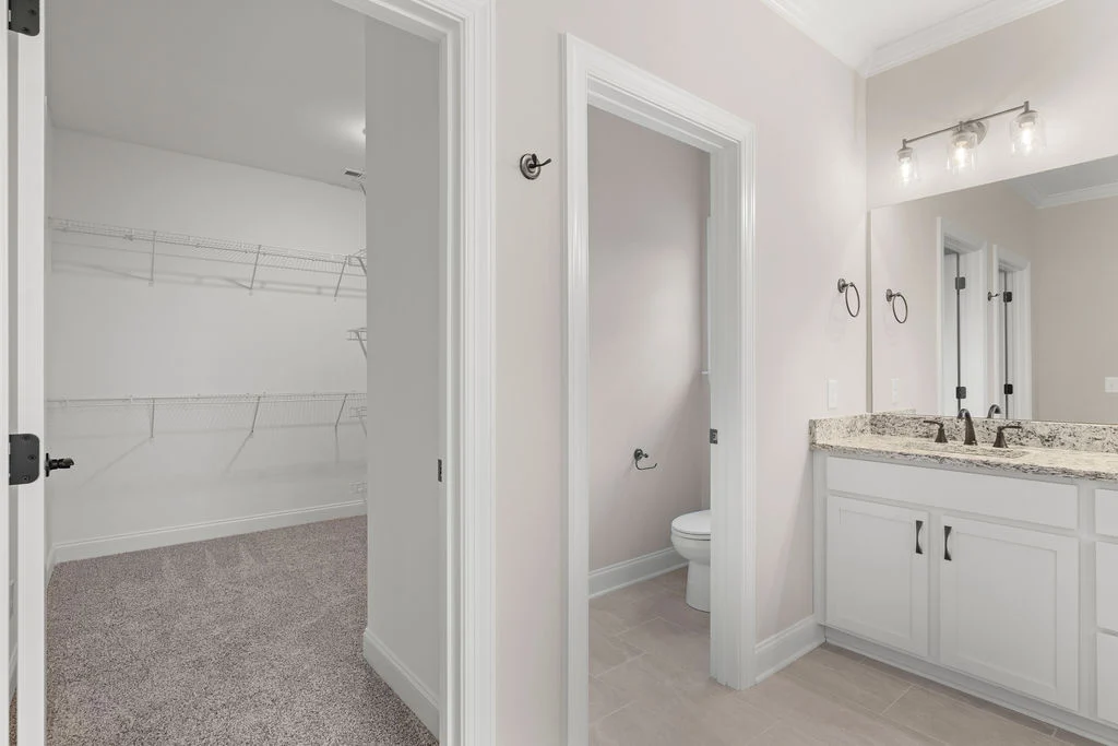 Modern bathroom with granite countertop and dual sinks adjacent to a spacious walk-in closet, designed by Pratt Home Builders in Chattanooga TN.