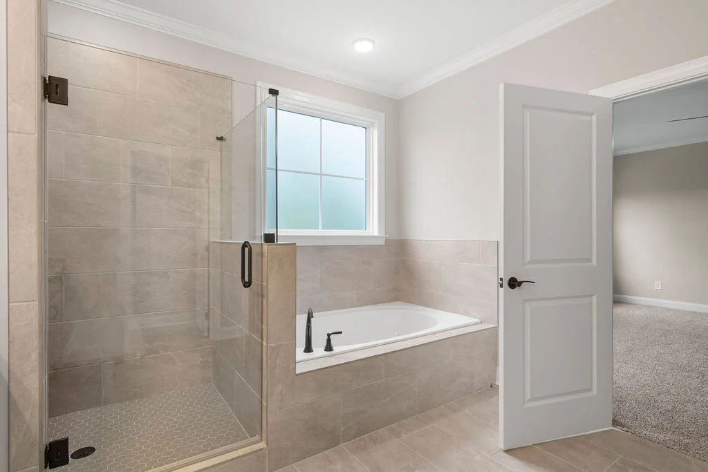 Modern bathroom with glass shower and bathtub. Neutral tiles and recessed lighting. Pratt Home Builders in Chattanooga TN design.