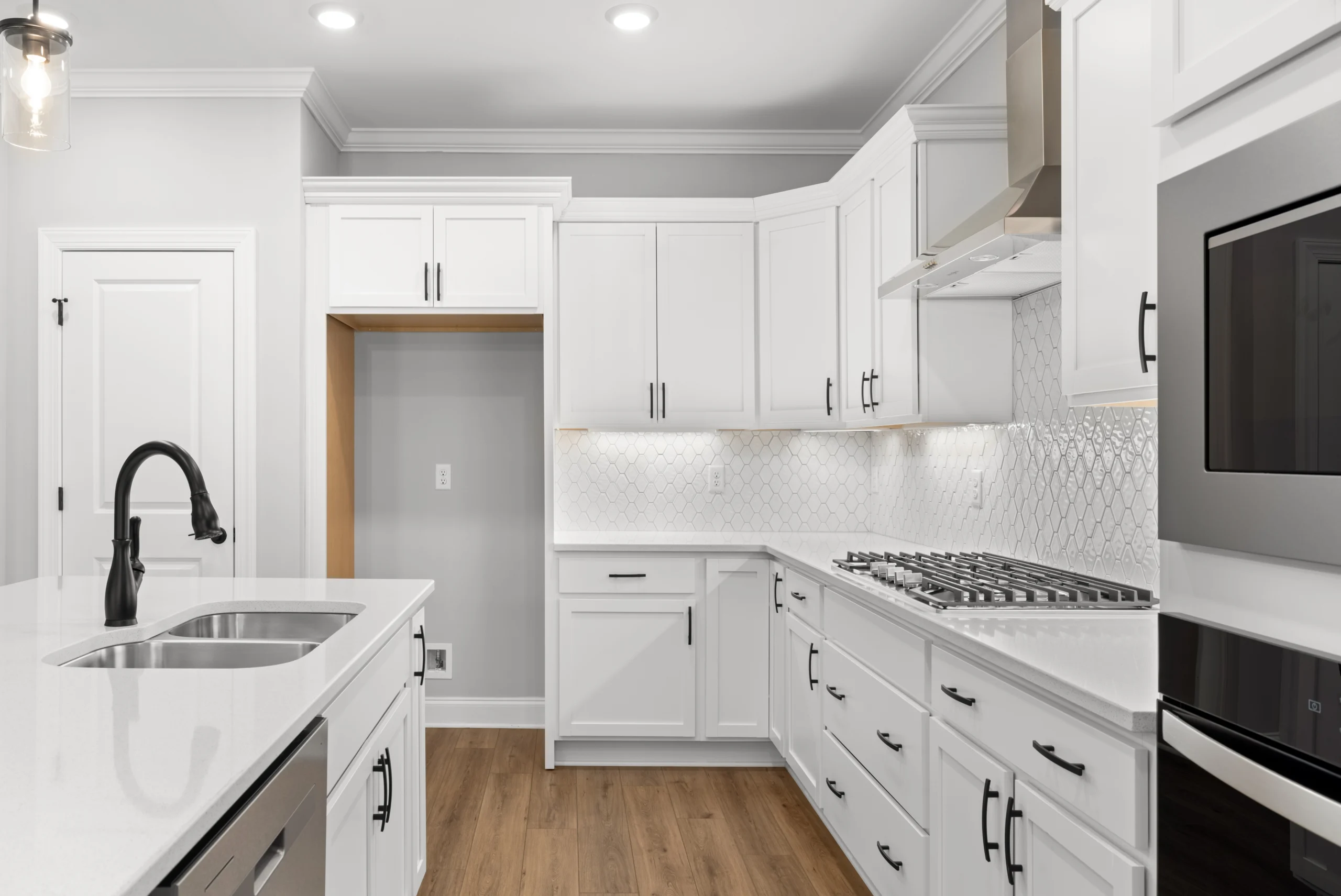 Modern kitchen by Pratt Home Builders in Chattanooga TN with white cabinets, hexagonal tile backsplash, stainless steel appliances, and wood flooring.