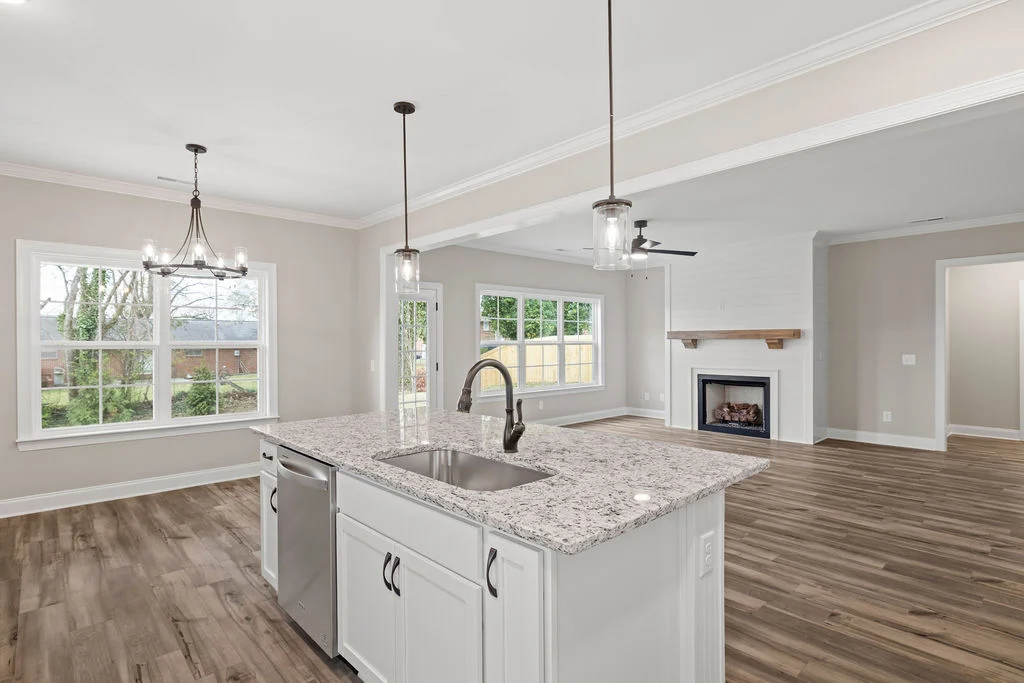 Modern kitchen and living area by Pratt Home Builders in Chattanooga TN, featuring granite island, pendant lights, hardwood floors, and fireplace.