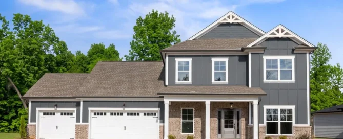 Modern two-story house with gray siding, brick accents, and three-car garage by Pratt Home Builders in Chattanooga, TN. Surrounded by trees, blue sky.