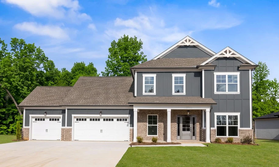 Modern two-story home with a three-car garage, gray siding, and brick accents by Pratt Home Builders in Chattanooga TN. Lush green surroundings.