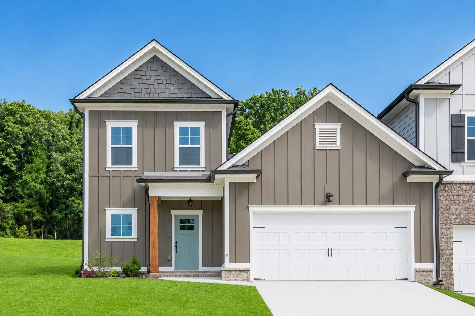 Two-story home with grey siding, white garage, and blue front door by Pratt Home Builders in Chattanooga, TN; green lawn and trees in background.