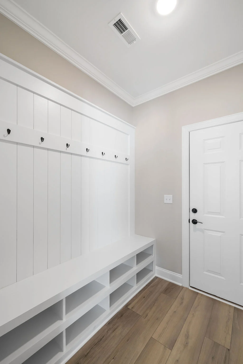 White mudroom with hanging hooks, bench, cubbies, and a door, designed by Pratt Home Builders in Chattanooga TN. Elegant and functional space.