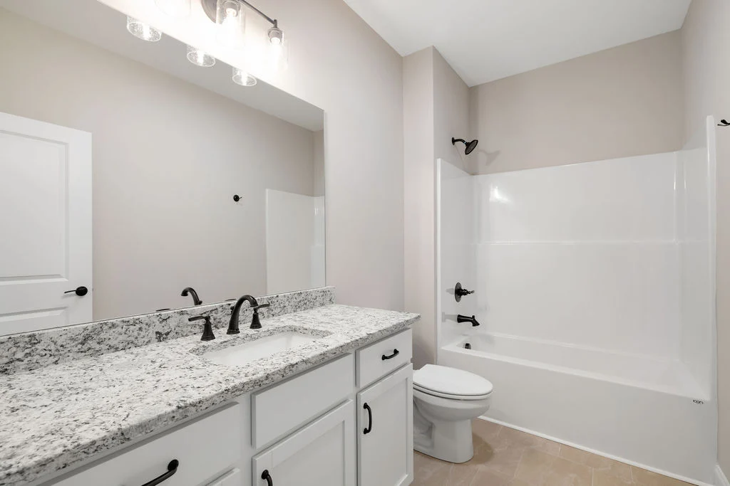 Modern bathroom by Pratt Home Builders in Chattanooga TN, featuring granite countertop, white cabinets, and a bathtub with black fixtures.