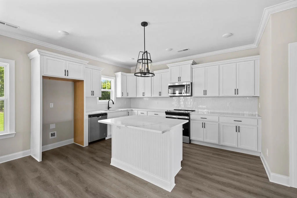 Modern kitchen with white cabinets, island, and stainless steel appliances by Pratt Home Builders in Chattanooga TN. Bright windows and wood floors.