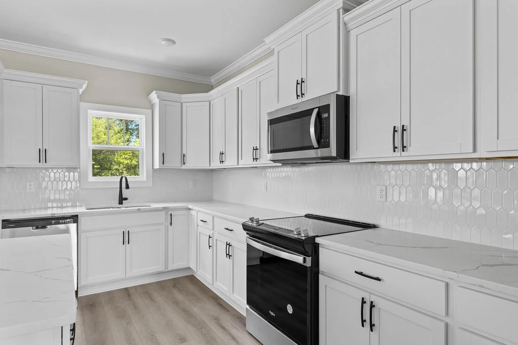 Modern kitchen with white cabinets, black appliances, and hexagonal tile backsplash by Pratt Home Builders in Chattanooga TN.