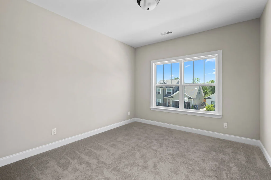 Empty room with beige walls, carpeted floor, and a window showing neighborhood view, built by Pratt Home Builders in Chattanooga TN.
