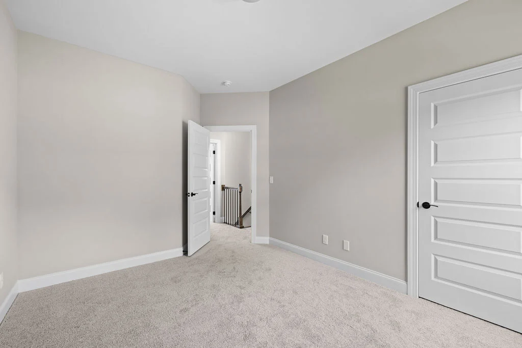 Neutral-colored room with carpet, white doors, and a view of a staircase. Built by Pratt Home Builders in Chattanooga, TN.