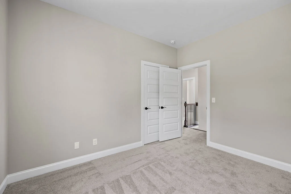 Empty room with beige walls, carpeted floor, and double white doors leading to a hallway by Pratt Home Builders in Chattanooga TN.