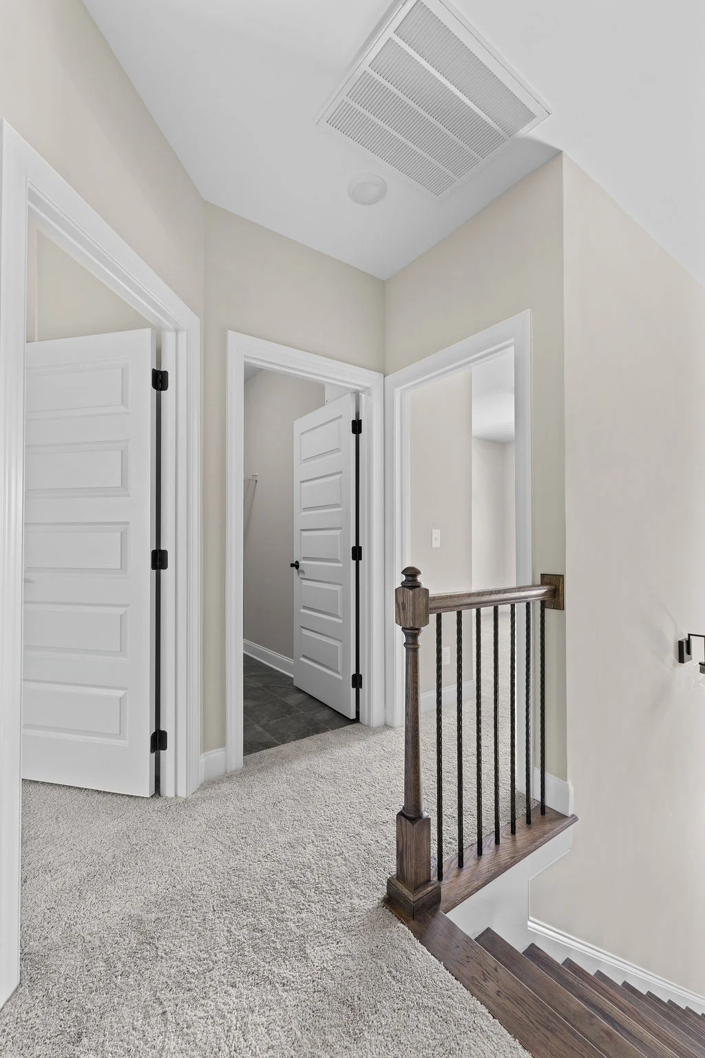 Bright hallway with white doors, beige walls, and carpeted flooring, leading to a staircase with wooden railing. Pratt Home Builders in Chattanooga TN