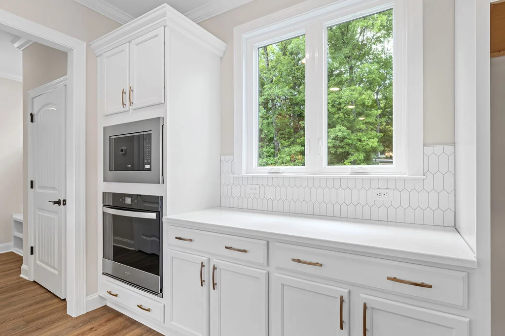 Bright, modern kitchen with white cabinetry, built-in oven, microwave, and large window. Pratt Home Builders in Chattanooga TN.