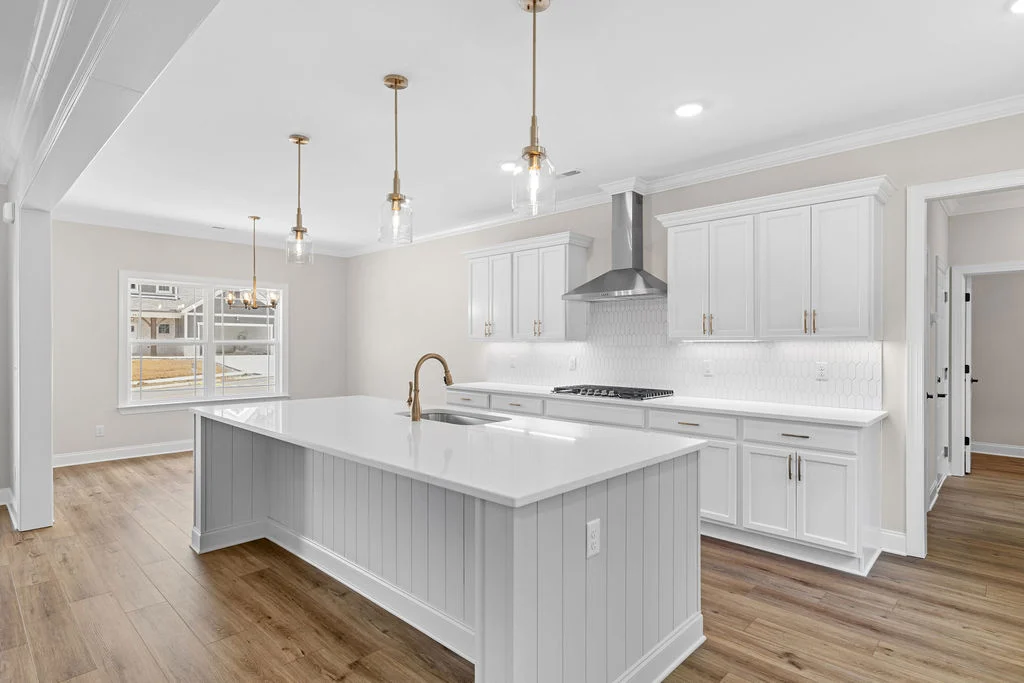 Bright kitchen with white cabinets, quartz island, pendant lights, and wide windows. Designed by Pratt Home Builders in Chattanooga TN.