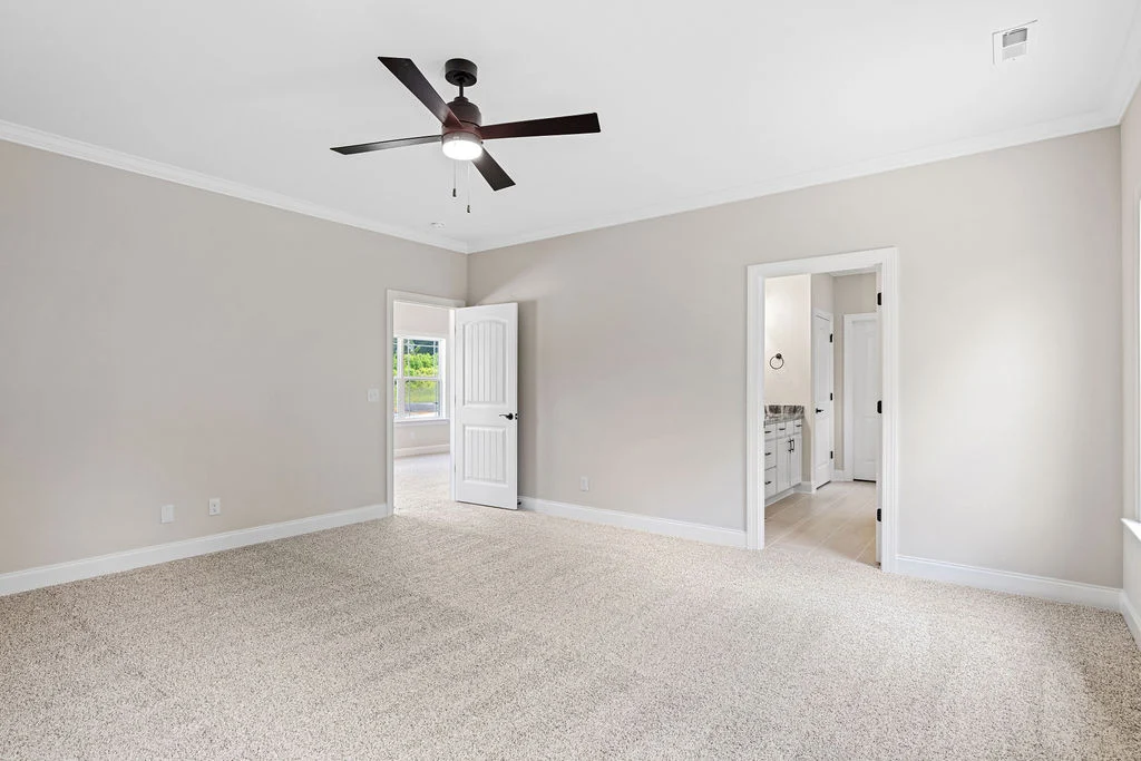 Spacious carpeted bedroom with ceiling fan, open doors to a bathroom and hallway, designed by Pratt Home Builders in Chattanooga TN.