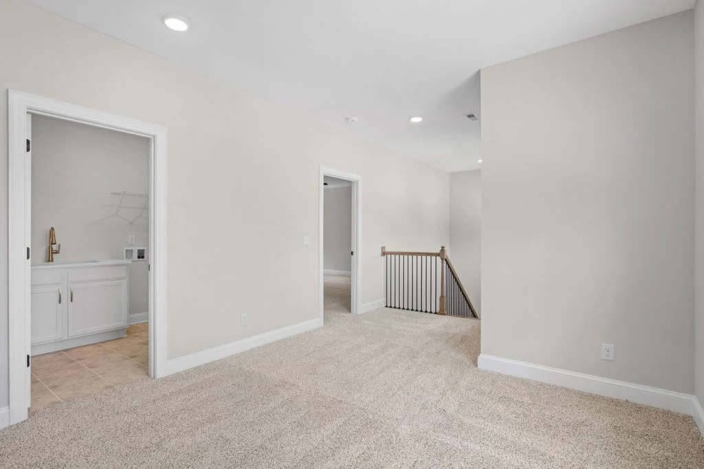 Hallway with beige carpet, cream walls, leading to rooms and a staircase. White cabinets visible in adjacent room. Pratt Home Builders in Chattanooga