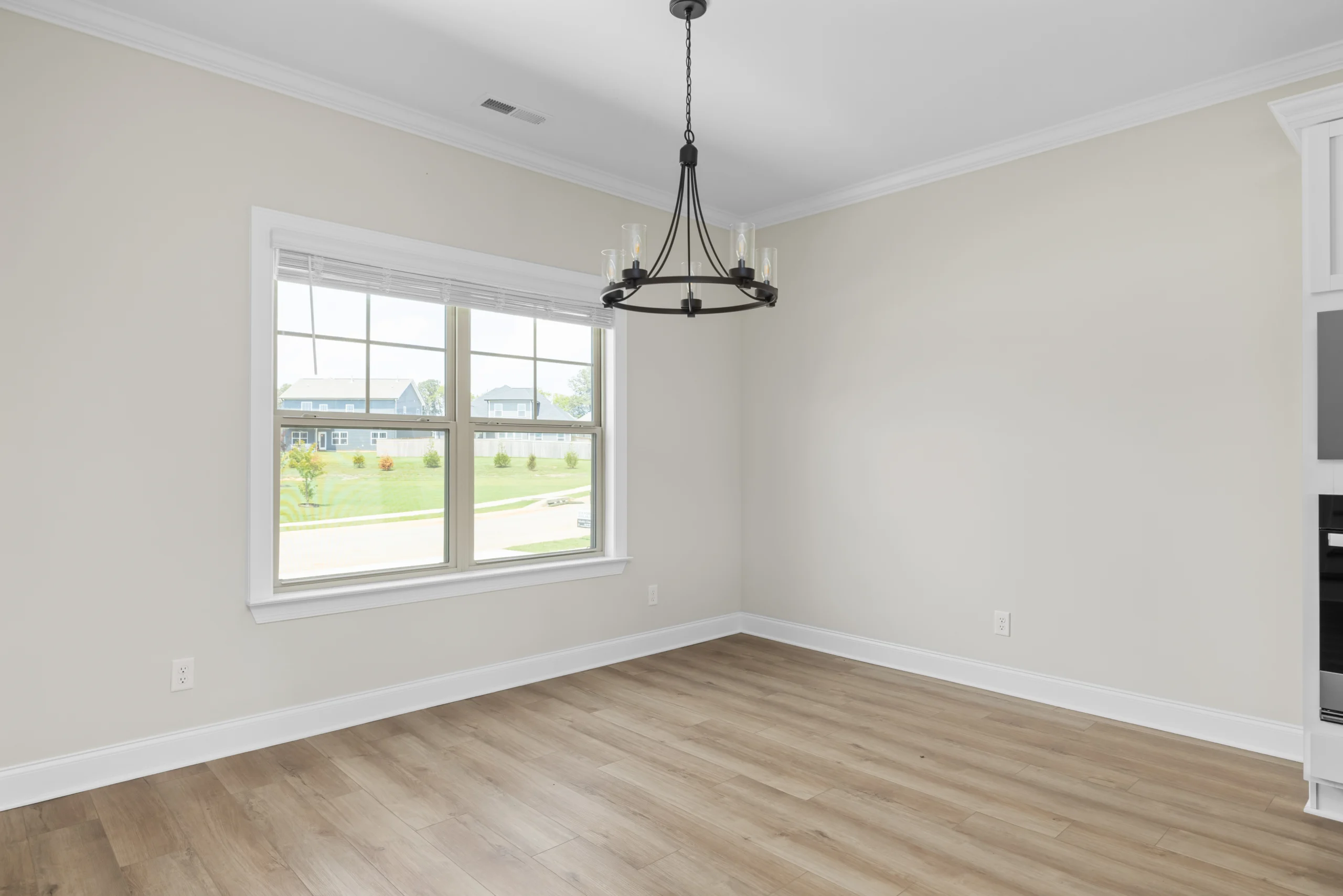 Bright empty room with wood flooring, large window, and chandelier by Pratt Home Builders in Chattanooga TN.