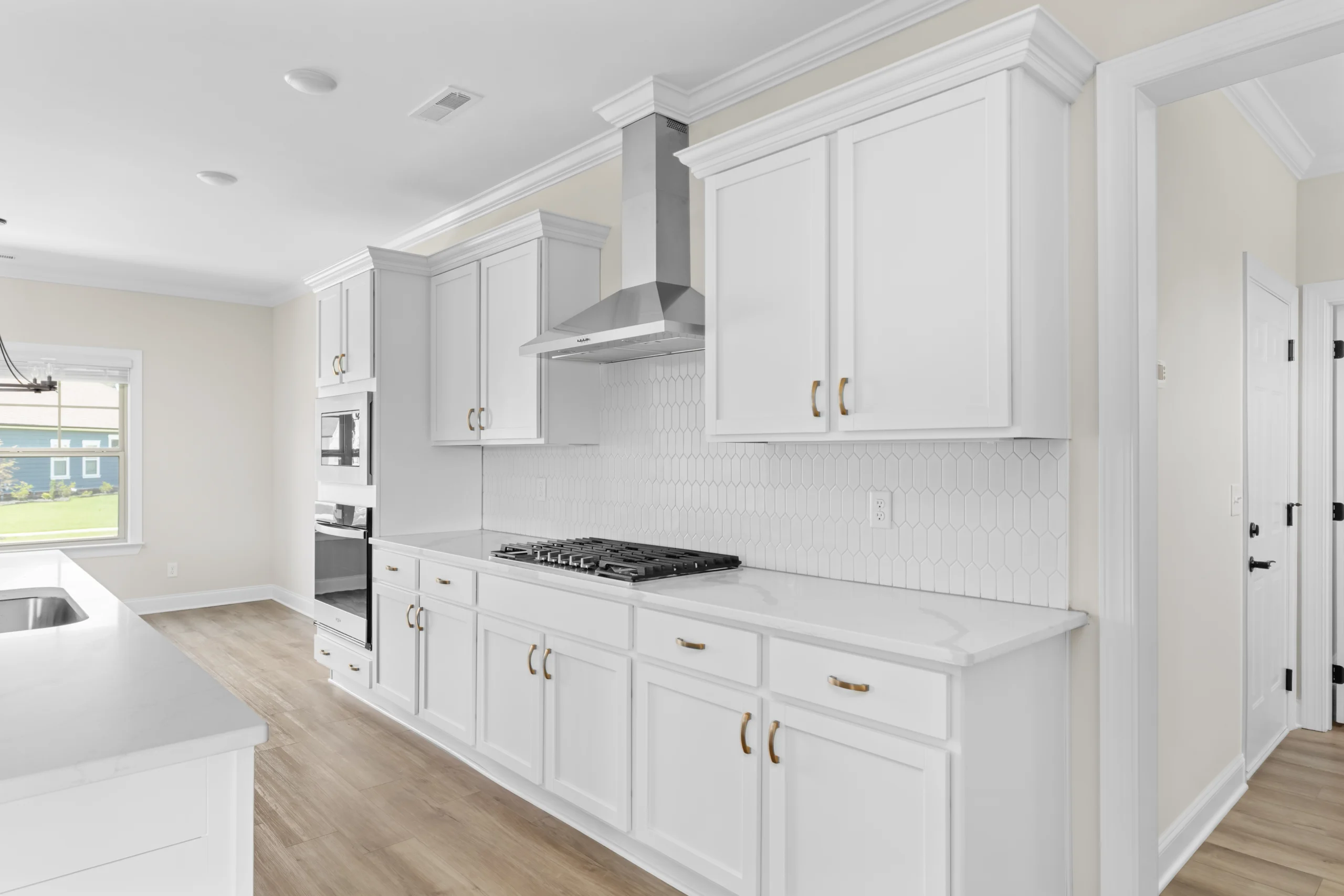 Modern kitchen with white cabinetry, stainless steel range hood, and wood flooring by Pratt Home Builders in Chattanooga TN.
