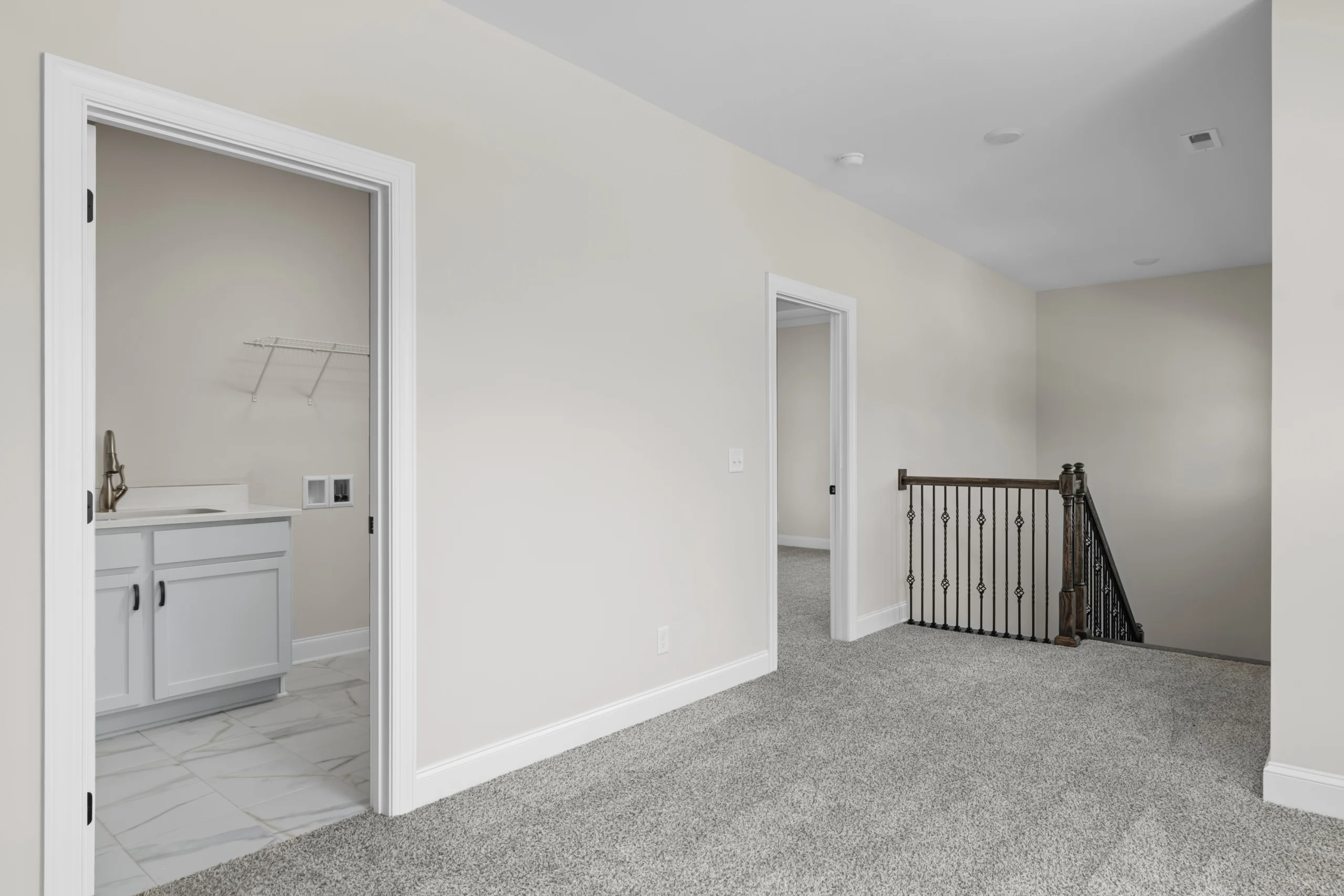 Modern hallway with plush carpet, two open doors, white cabinets, and black stair railing. Built by Pratt Home Builders in Chattanooga TN.