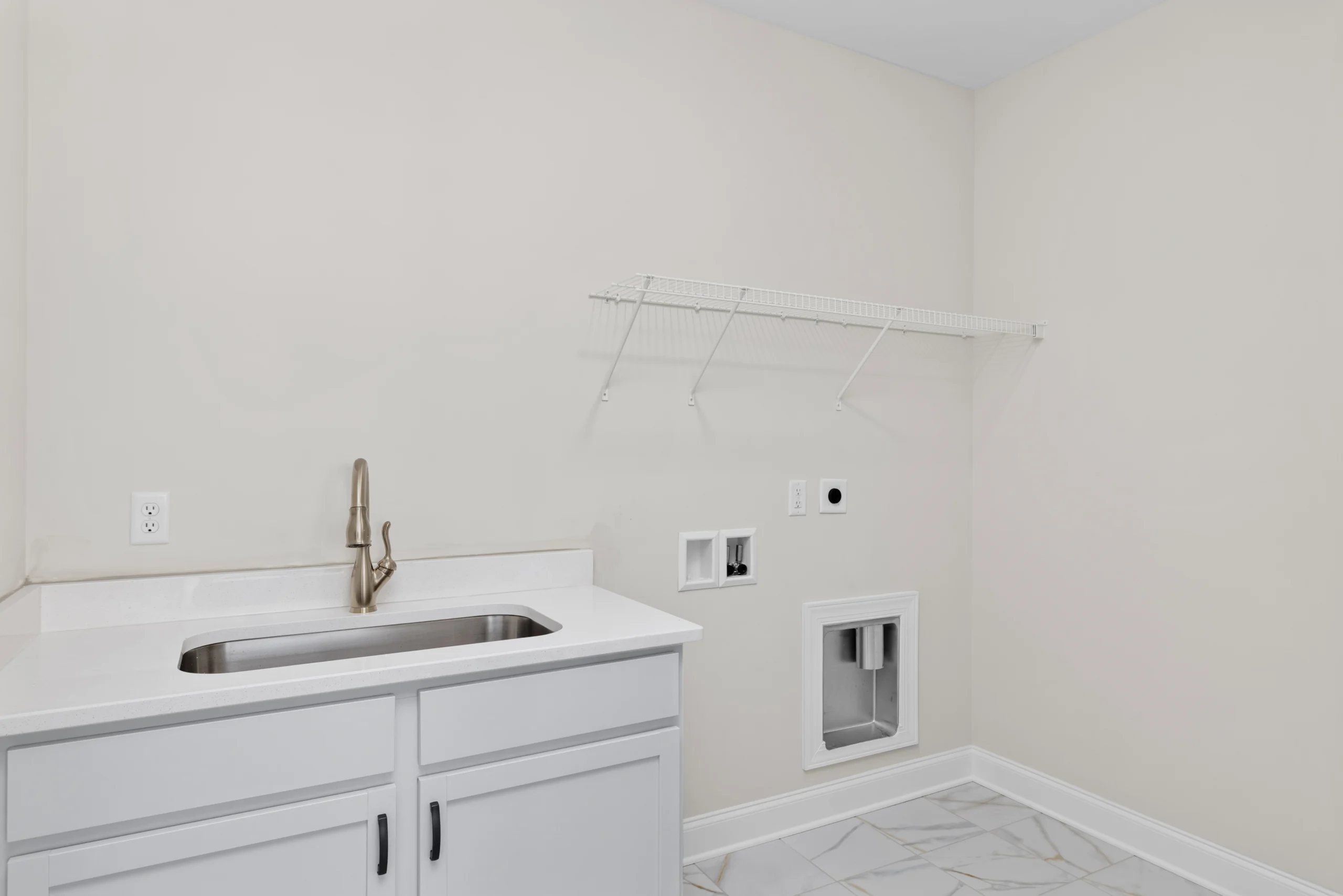 Modern laundry room by Pratt Home Builders in Chattanooga TN, featuring a sleek sink, white cabinets, and tiled floor with ample wall shelving.
