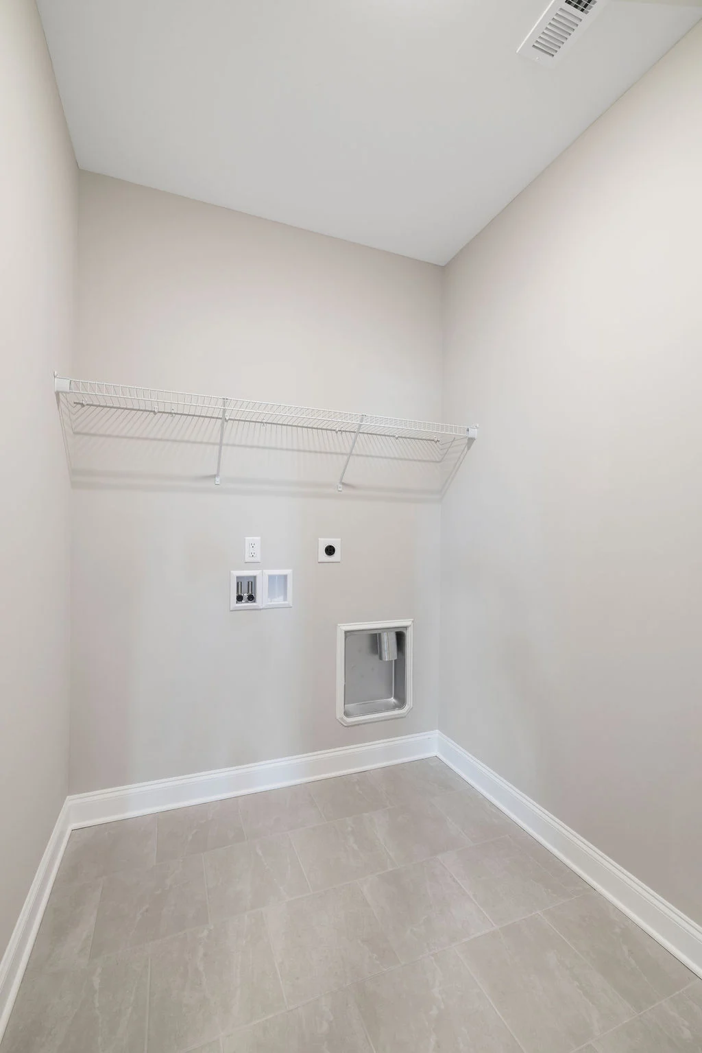 Empty laundry room with washer and dryer hookups, wire shelf, and beige walls by Pratt Home Builders in Chattanooga TN.