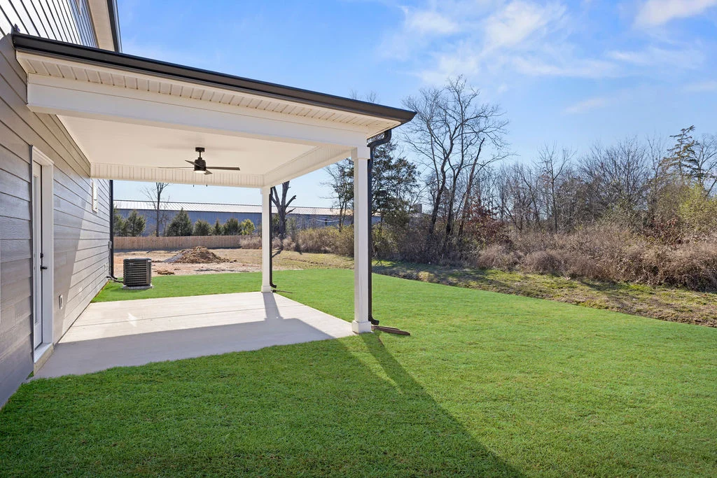 Covered backyard patio with ceiling fan, overlooking a grassy yard beside a wooded area, designed by Pratt Home Builders in Chattanooga TN.
