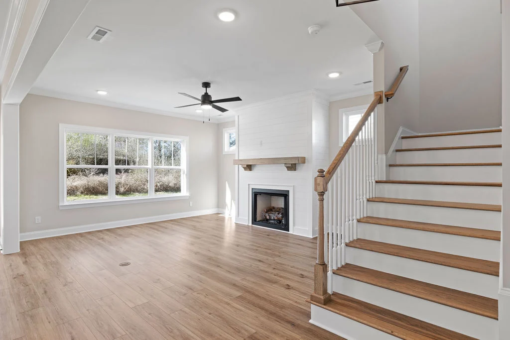 Spacious living area by Pratt Home Builders in Chattanooga TN, featuring hardwood floors, ceiling fan, fireplace, and staircase.