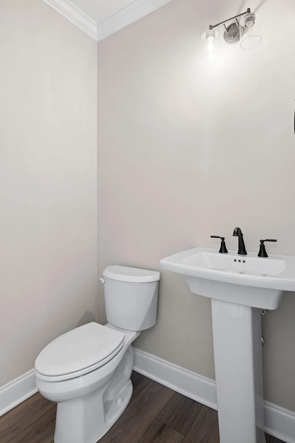 Elegant bathroom with white pedestal sink, modern black fixtures, and toilet on wood floor by Pratt Home Builders in Chattanooga TN.