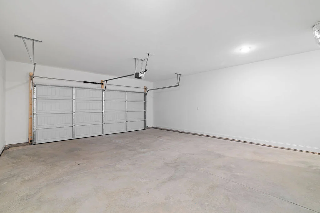 Spacious, empty garage with a closed double door and smooth concrete floor, designed by Pratt Home Builders in Chattanooga TN.