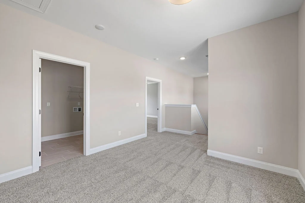 Spacious landing area with carpeted floor, beige walls, and access to laundry room, designed by Pratt Home Builders in Chattanooga TN.