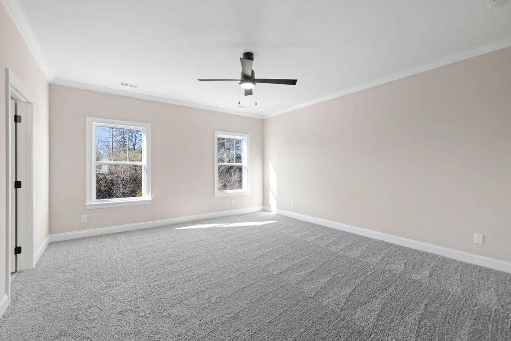 Spacious, carpeted room with light gray walls, two large windows, modern ceiling fan. Built by Pratt Home Builders in Chattanooga TN.