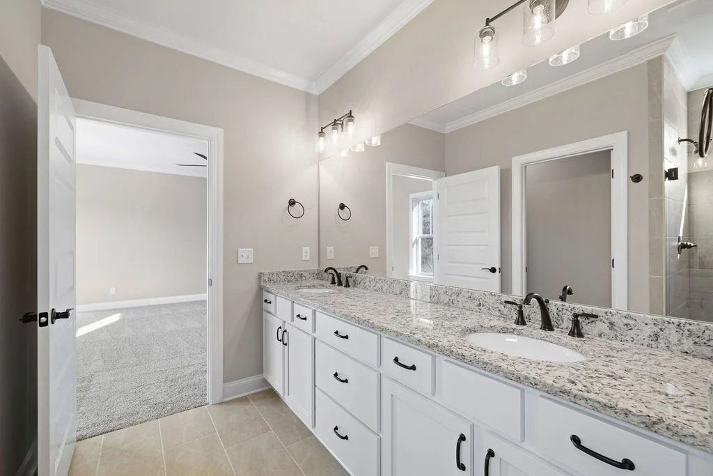 Modern bathroom with granite countertop, dual sinks, elegant lighting, and beige walls by Pratt Home Builders in Chattanooga TN.