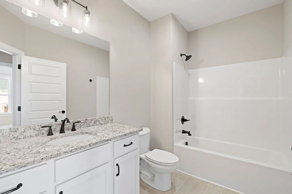 Modern bathroom with granite countertop, single sink, white cabinetry, and combined shower-tub. Built by Pratt Home Builders in Chattanooga, TN.
