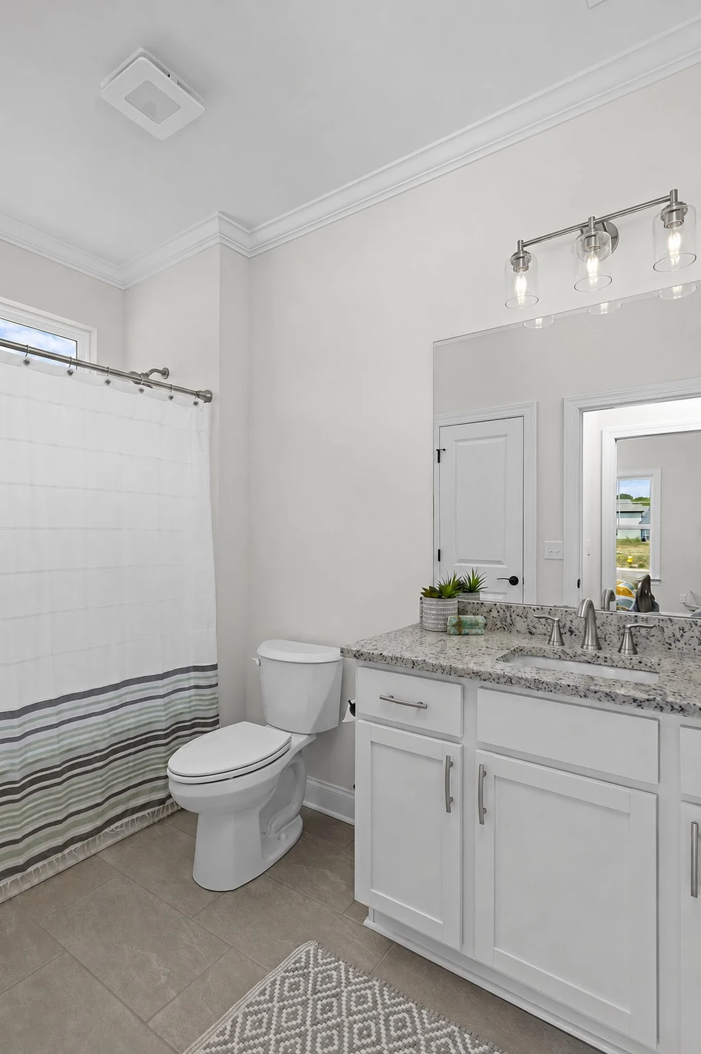 Bathroom with granite countertop, double sink, and chrome fixtures. Shower with striped curtain. Built by Pratt Home Builders in Chattanooga TN.