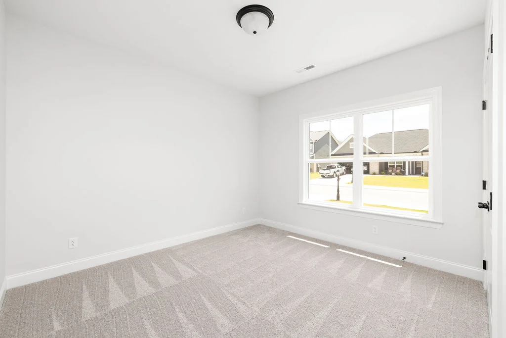 Bright, empty room with soft carpet, large window showing suburban street. Interior crafted by Pratt Home Builders in Chattanooga TN.