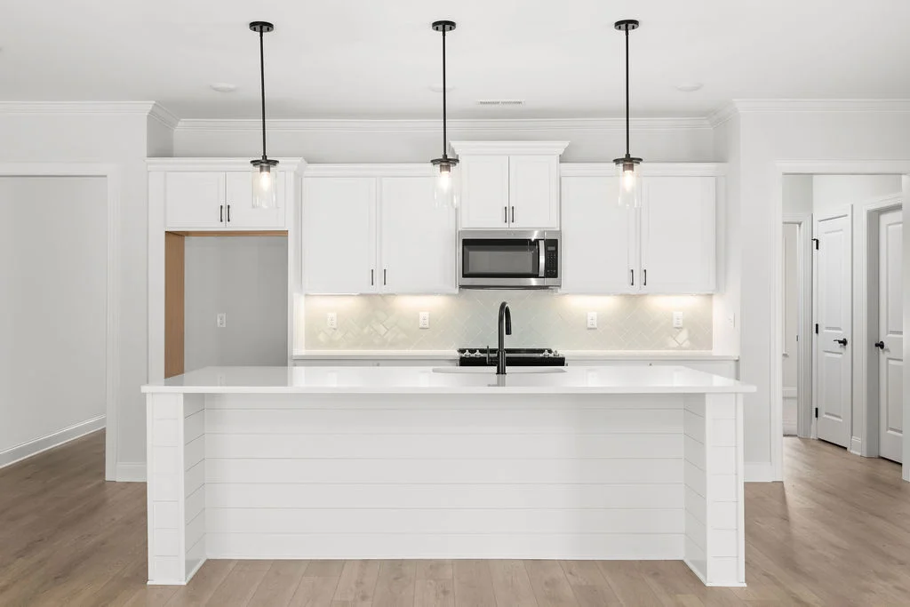 Modern white kitchen by Pratt Home Builders in Chattanooga TN, featuring a sleek island, pendant lighting, and stainless steel appliances.