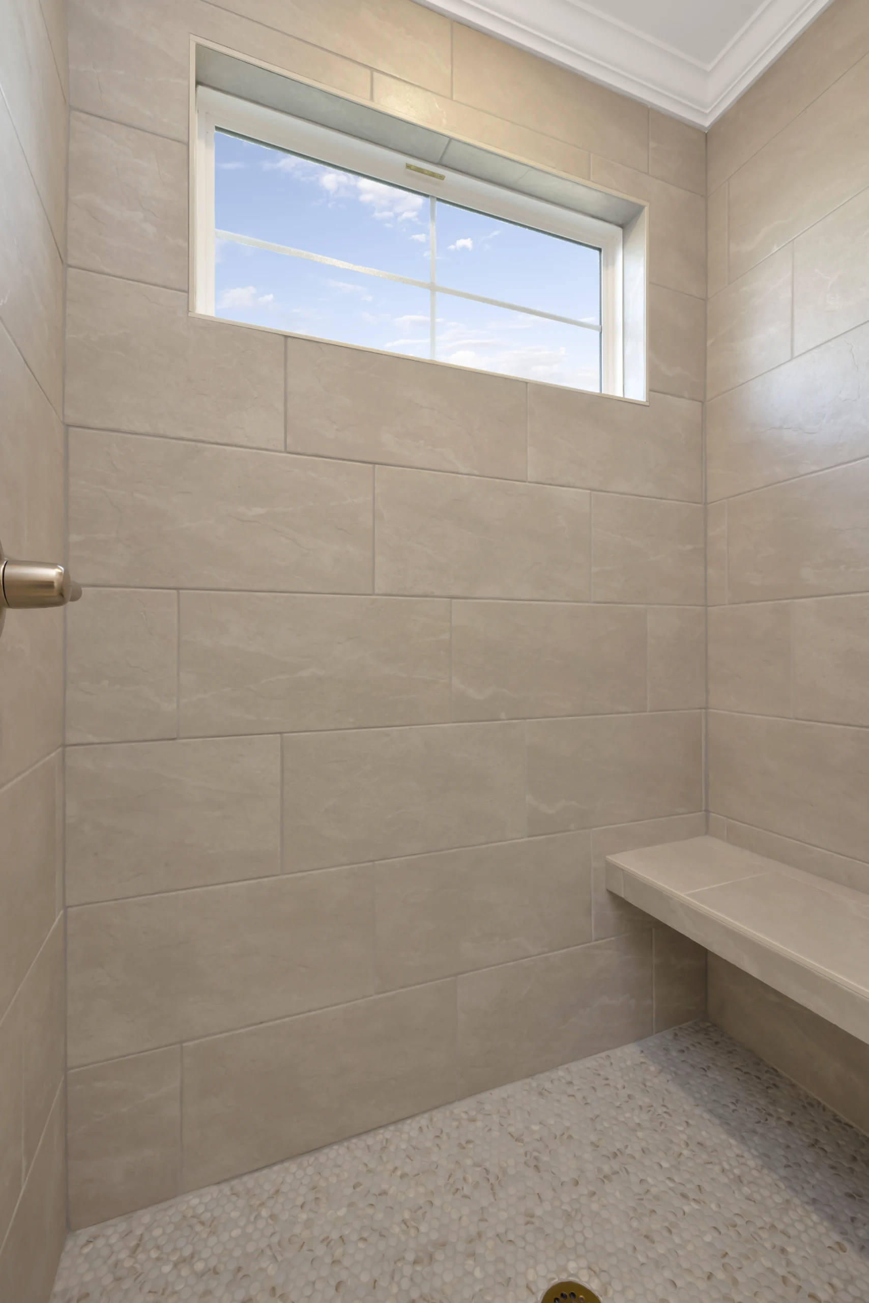 Beige tiled shower with corner bench and small window, showcasing Pratt Home Builders in Chattanooga TN.