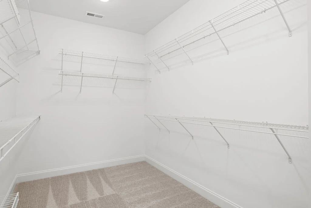 Spacious white walk-in closet with wire shelving, by Pratt Home Builders in Chattanooga TN. Beige carpet floor.