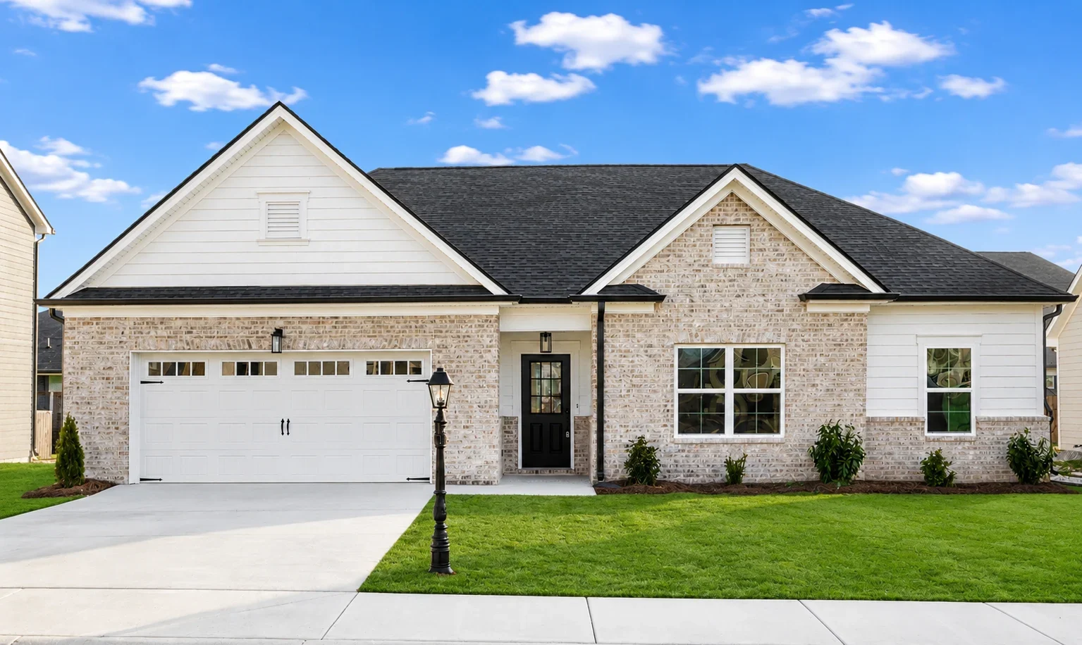 Single-story brick house with black roof, white garage, manicured lawn, and a vintage lamp post, by Pratt Home Builders in Chattanooga TN.