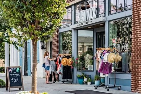 Shopping Woman shops outside a boutique with clothing racks and hats. Brick exterior and sidewalk visible. Pratt Home Builders in Chattanooga TN nearby.