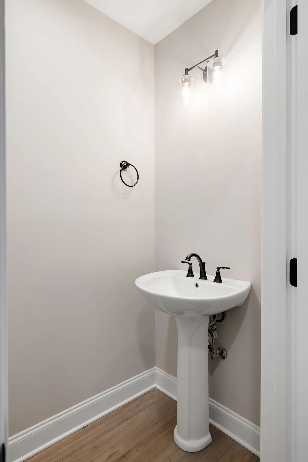 Modern bathroom with pedestal sink, sleek black fixtures, and wood flooring. Designed by Pratt Home Builders in Chattanooga TN.