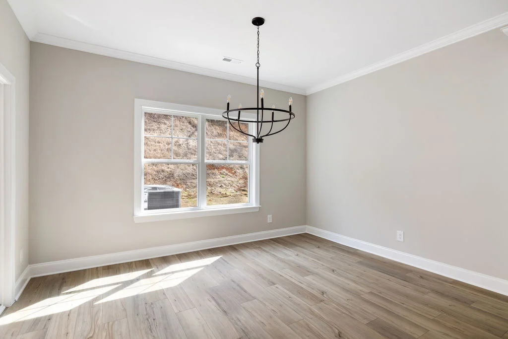 Bright, empty room with light wood flooring, beige walls, large window, and modern chandelier. Built by Pratt Home Builders in Chattanooga TN.